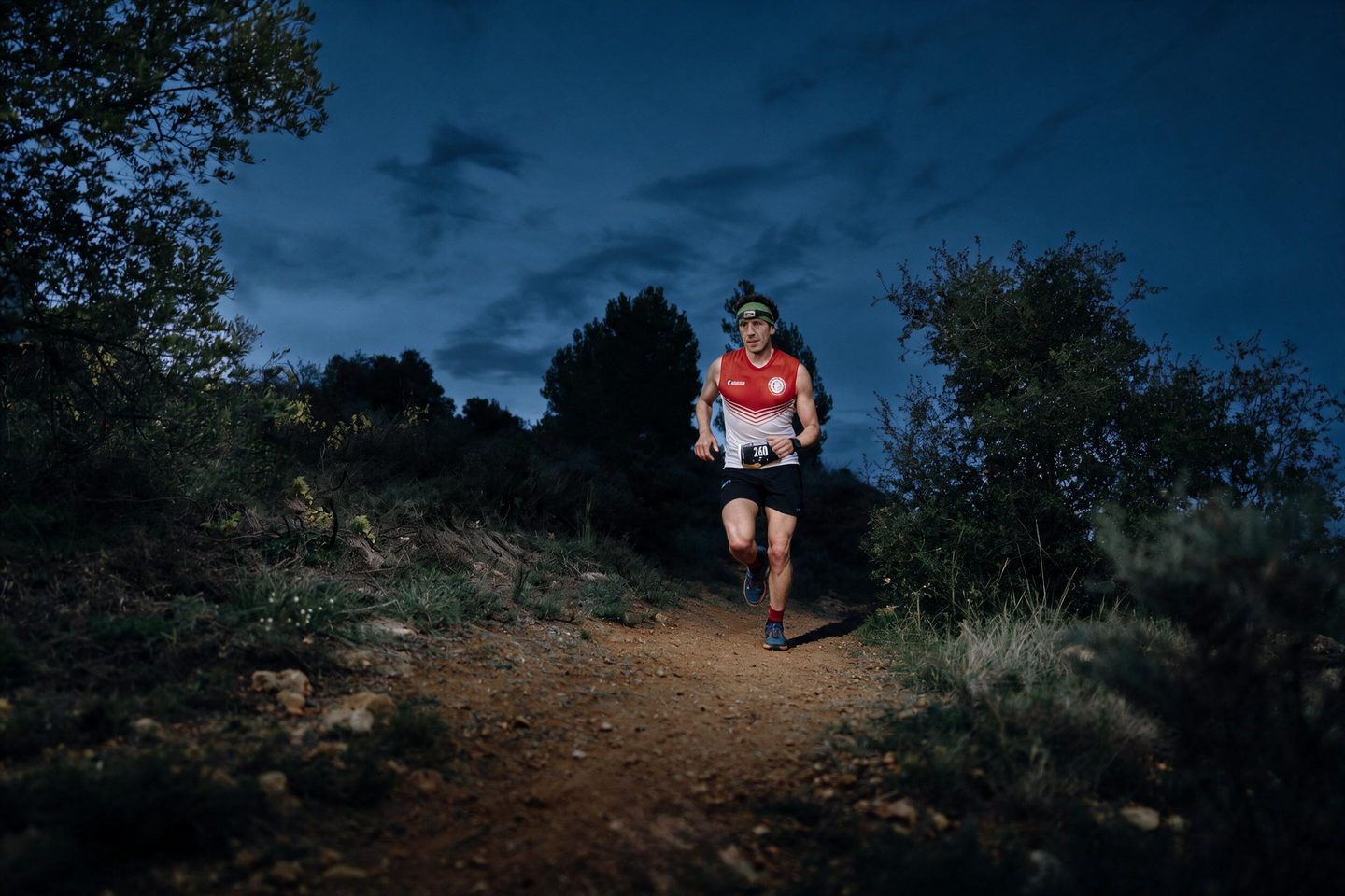 Un corredor amb frontal per un corriol de carena, de nit, amb el cel blau fosc al fons